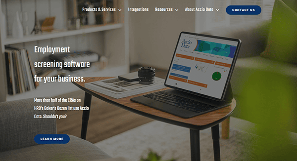 A laptop rests on the table, showcasing employment screening software on Accio Data's website, one of the best background check websites. The inviting background reveals a cozy couch and shelves adorned with books and decor.