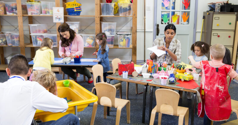 Children and adults in the best daycare engage in various activities, including painting, crafting, and working with water. Colorful handprints decorate a door in the background.