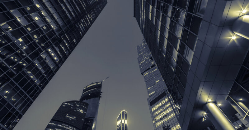 View from below of modern skyscrapers with lit windows against a dusky sky, reflecting the allure of urban architecture often showcased on commercial real estate websites.