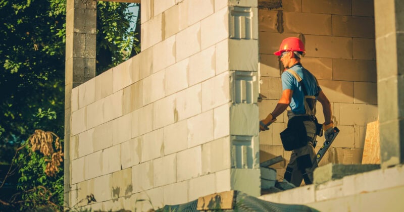 A person in a red hard hat navigates through a partially constructed building, carrying tools with precision. As the industry anticipates the rise of digital-first buyers by 2025, this scene embodies the evolving landscape of home builder marketing.