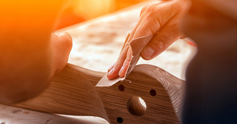 A person sanding a wooden piece with a hole in it, capturing the intricate details of furniture refinishing under warm sunlight.