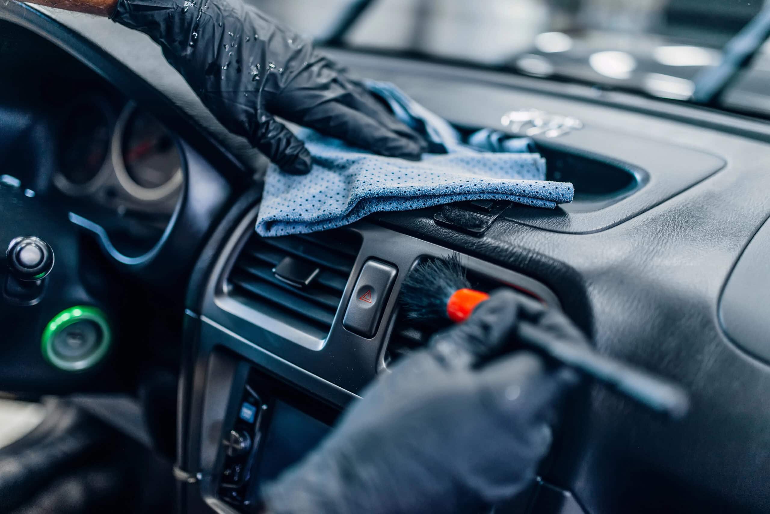 A person, deeply engrossed in auto detailing, meticulously cleans a car dashboard with gloves, using a cloth and brush to achieve that perfect shine.