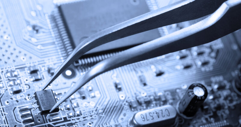 Tweezers hold a small electronic component above a circuit board, a crucial step in any computer repair process.