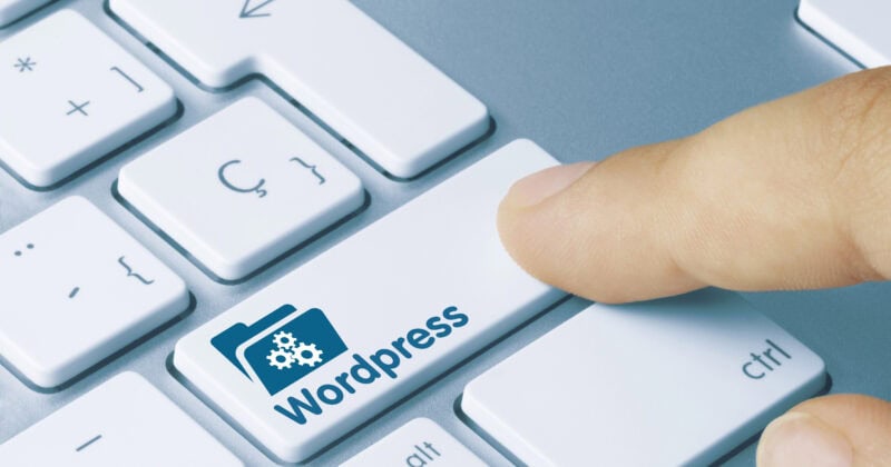 A finger pressing a white keyboard key labeled with a blue WordPress icon and the text "Wordpress.