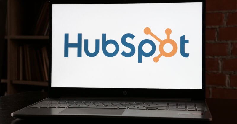 A laptop screen showcasing the HubSpot logo, set against a backdrop of a bookshelf and red brick wall, offers an inviting view. Discover the benefits of seamless transitions with our comprehensive guide on HubSpot to WordPress migration.