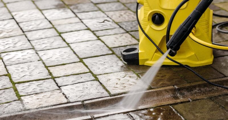 A yellow pressure washer is expertly spraying water to clean a wet, tiled outdoor surface, demonstrating the efficiency of pressure washing.