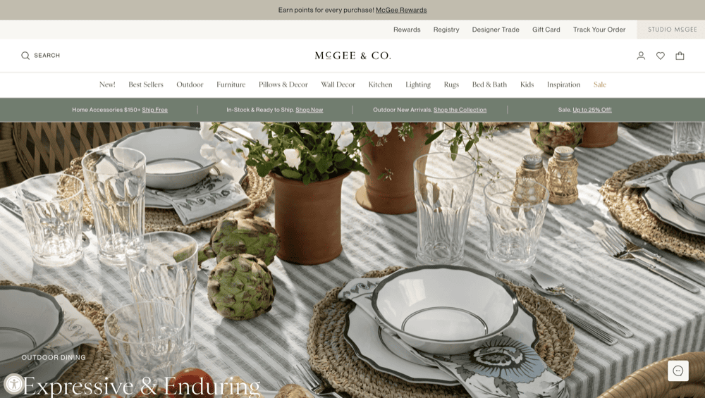 A dining table set with glassware, plates, and floral-patterned napkins on a striped tablecloth elegantly showcases the latest trends from top home decor websites. Wicker placemats and decorative artichokes complete the 2025-inspired look.